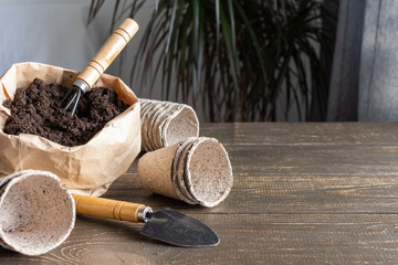 Eco friendly pots for seedlings on wooden background, small bag with ground and garden trowel and...