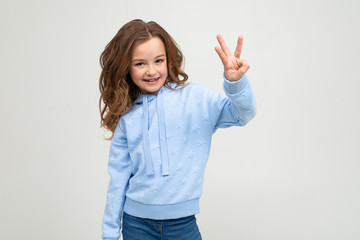 charming teen girl in a blue hoodie shows three fingers on a light gray background