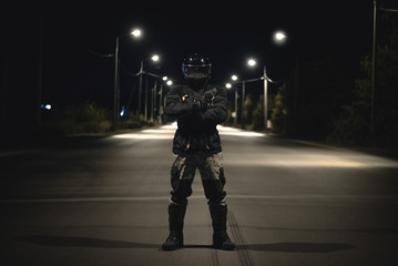 Serious motorcyclist standing with crossed arms on a night road background.