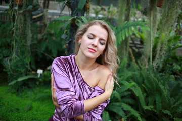  beautiful girl with long white hair in violet velvet top and lilac light fanin skirt enjoys nature in the garden