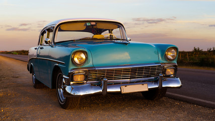 Fototapeta na wymiar old vintage baby blue classic car with white top at sunset, cuba