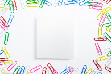 Colorful paper clips and portrait paper frame in the centre of composition isolated on white.