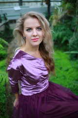 Fototapeta premium beautiful girl with long white hair in violet velvet top and lilac light fanin skirt enjoys nature in the garden