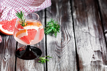 Refreshing drink with grapefruit and rosemary in a glass on a wooden rustic table. Selective focus, copy space. Summer cold cocktail.