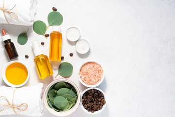 Organic ingredients for homemade cosmetics. Spa and wellness concept. Essential oils, eucalyptus leaves, honey and Himalaya salt on white marble table with copy space for your design.