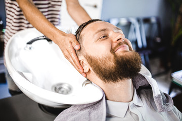 wash your hair in a hair salon. A man with a beard is sitting in a Barber chair washing his head in...
