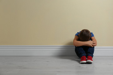 Little boy on floor near yellow wall, space for text. Child in danger