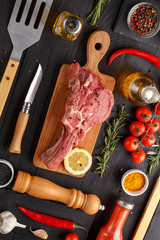 Raw beef antricot on a wooden board. Composition with rosemary, hot pepper and other spices for cooking meat. A look from above.