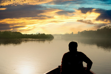 silhouette of boatsman rowing out into the yamuna ganga river in the morning