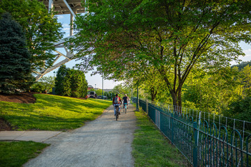People riding bicycles on a path, under green trees. A place for relaxation and activities. Pittsburgh, Pennsylvania, USA. - obrazy, fototapety, plakaty
