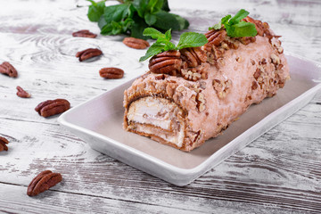 Meringue roulade with pecan nuts and cream cheese filling on the ceramic platter on the white wooden table