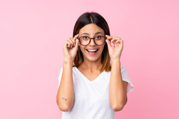 Young woman over isolated pink background with glasses and surprised