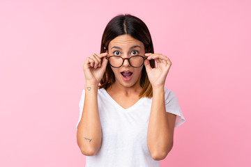Young woman over isolated pink background with glasses and surprised - obrazy, fototapety, plakaty
