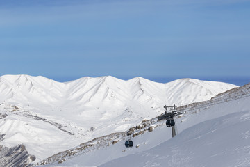 Snowy sunlit mountains and gondola lift at ski resort at sunny winter evening.