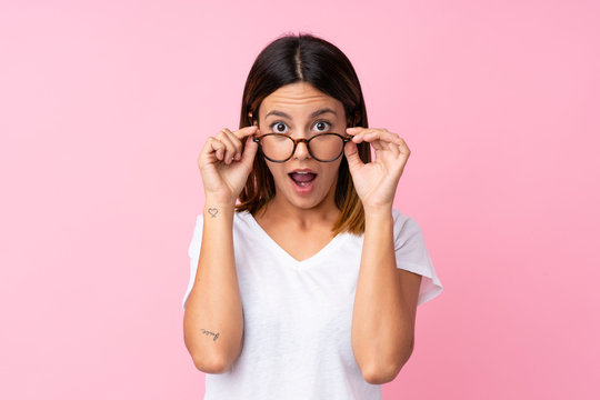 Young woman over isolated pink background with glasses and surprised