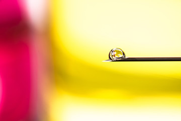 Drop on a medical needle. Macro photo of injection or vaccination solution on a colored background.