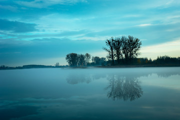 Wonderful fog on the lake and trees reflecting in the water, evening view