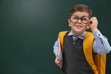 Cute little child wearing glasses near chalkboard, space for text. First time at school