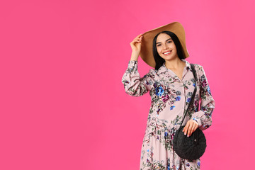 Young woman wearing floral print dress and straw hat on pink background. Space for text