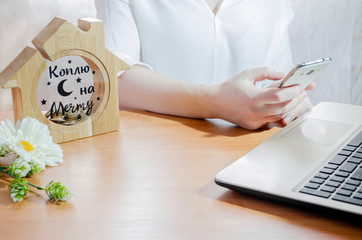 wooden piggy bank with the inscription "saving up for a dream" in the form of a house on the desktop and a girl at the table