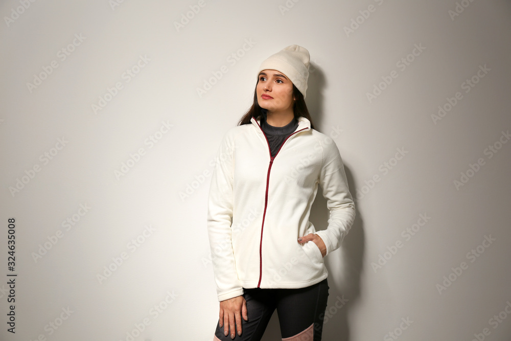 Sticker Woman wearing fleece jacket and hat on light grey background. Winter sport clothes