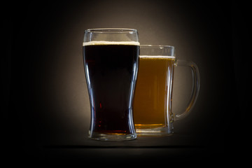 Glass of dark and light beer on black background with spotted light