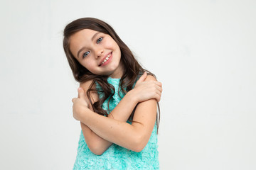 beautiful teenager girl in a blue dress hugs herself on a white studio background