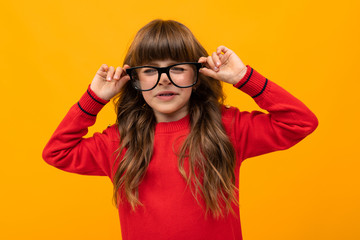 Beautiful little girl in dress plays with glasses isolated on yellow and orange background