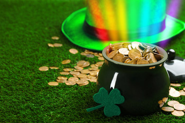 Pot with gold coins, hat and clover on green grass, space for text. St. Patrick's Day celebration