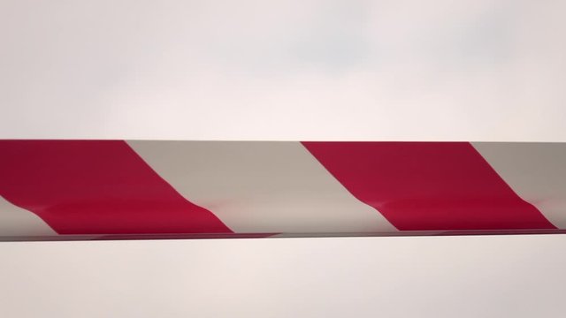 Striped protective tape on the wind in slow motion against white sky background. Warning ribbon. Red and white stope line. Keep out. Dangerous. Close up shot. 
