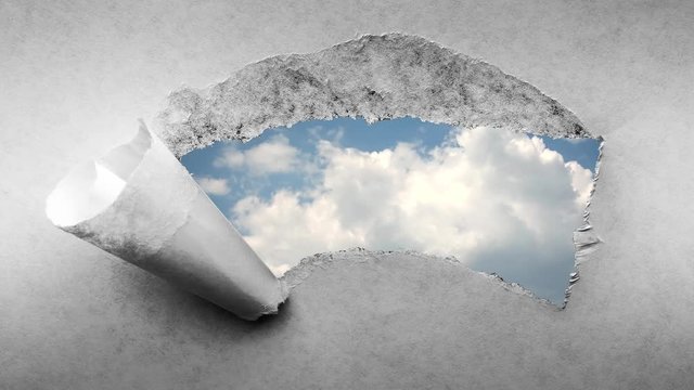 Creative 4k time laps video of fast moving clouds in the blue sky that are visible through a hole with torn edges in old retro grunge vintage paper.