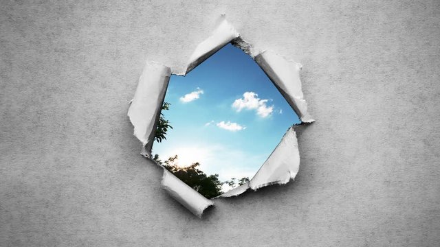 Creative 4k time laps video of fast moving clouds in the blue sky that are visible through a hole with torn edges in old retro grunge vintage paper.