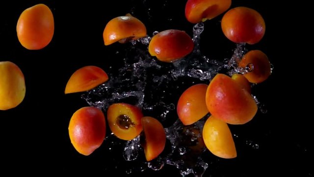 Delicious juicy apricot halves are flying up with a water splashes on a black background in slow motion