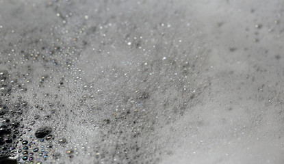 A lot of dish soup foam bubbles on top of water while hand washing dishes. Beautiful white, shiny bubble texture. Lovely background photo. Closeup color image.