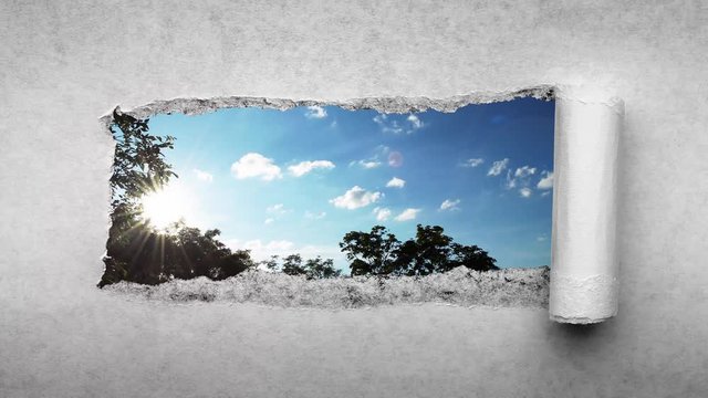 Creative 4k time laps video of fast moving clouds in the blue sky at sunset witn sunflare that are visible through a hole with torn edges in old retro grunge vintage paper.