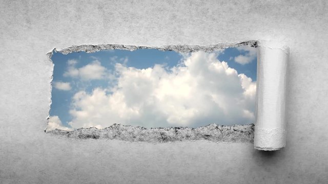 Creative 4k time laps video of fast moving clouds in the blue sky that are visible through a hole with torn edges in old retro grunge vintage paper.