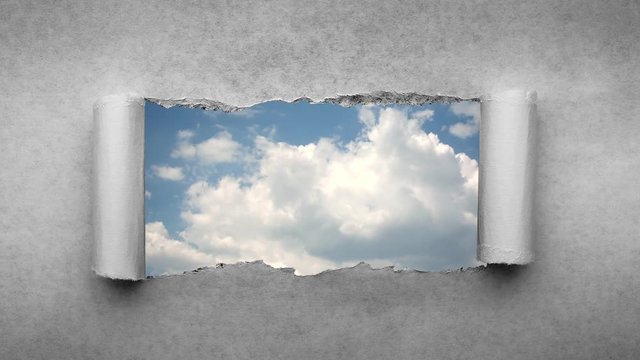 Creative 4k time laps video of fast moving clouds in the blue sky that are visible through a hole with torn edges in old retro grunge vintage paper.
