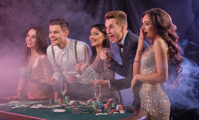 Friends playing poker at casino, at table with stacks of chips, money, cards, champagne on it....