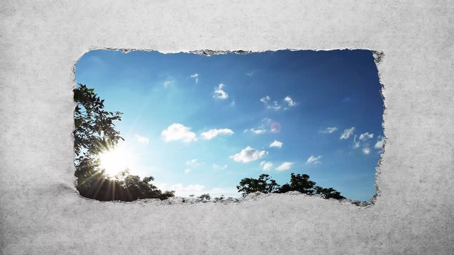 Creative 4k time laps video of fast moving clouds in the blue sky at sunset witn sunflare that are visible through a hole with torn edges in old retro grunge vintage paper.