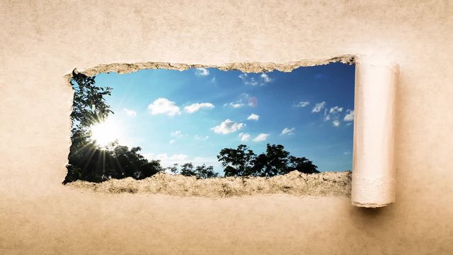 Creative 4k time laps video of fast moving clouds in the blue sky at sunset witn sunflare that are visible through a hole with torn edges in old retro grunge vintage paper.