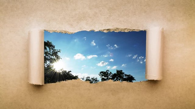 Creative 4k time laps video of fast moving clouds in the blue sky at sunset witn sunflare that are visible through a hole with torn edges in old retro grunge vintage paper.