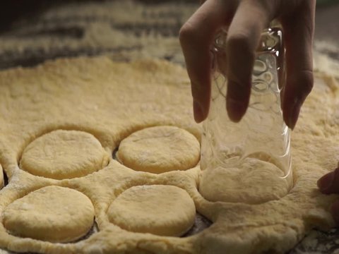woman kneading dough, making round shapes with a glass to make a doughnuts at the kitchen table