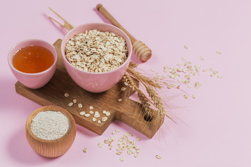 Bowl of dry oat flakes with honey, oatmeal and ears of wheat on light background. Healthy skin,...
