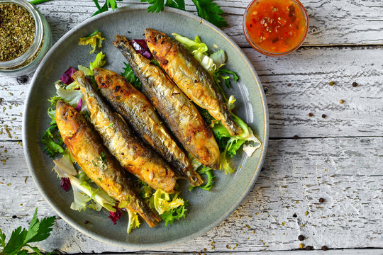 Grilled fish in a gray plate. Small fried fish and salad dressing. Top view. Wood background