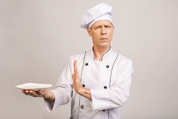 Senior male chef cook or baker man in white uniform posing isolated on white background. Cooking food concept. Showing stop gesture to plate.