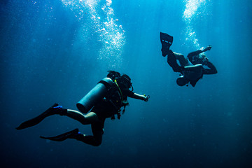 Scuba diver reaching its diving partner in deep blue sea