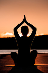 Silhouette of female adult sitting in lotus position with hands in namaste