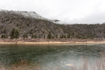 Calm green river in front of tree covered mountain shrouded in fog