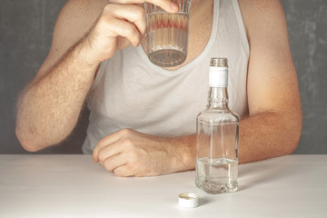 A lone man, an alcoholic without a face in a white T-shirt, sits at a table and drinks vodka from a faceted glass.
