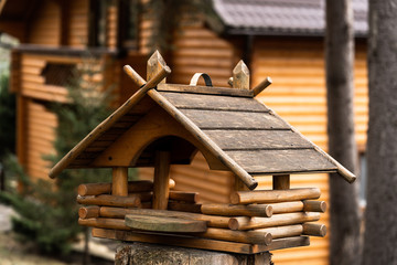 Obraz na płótnie Canvas Birdhouse on a tree hanging from a branch. Wooden birdhouse made of small logs. Birdhouse on blurred city background. Handcrafted log cabin birdhouse. Save animals